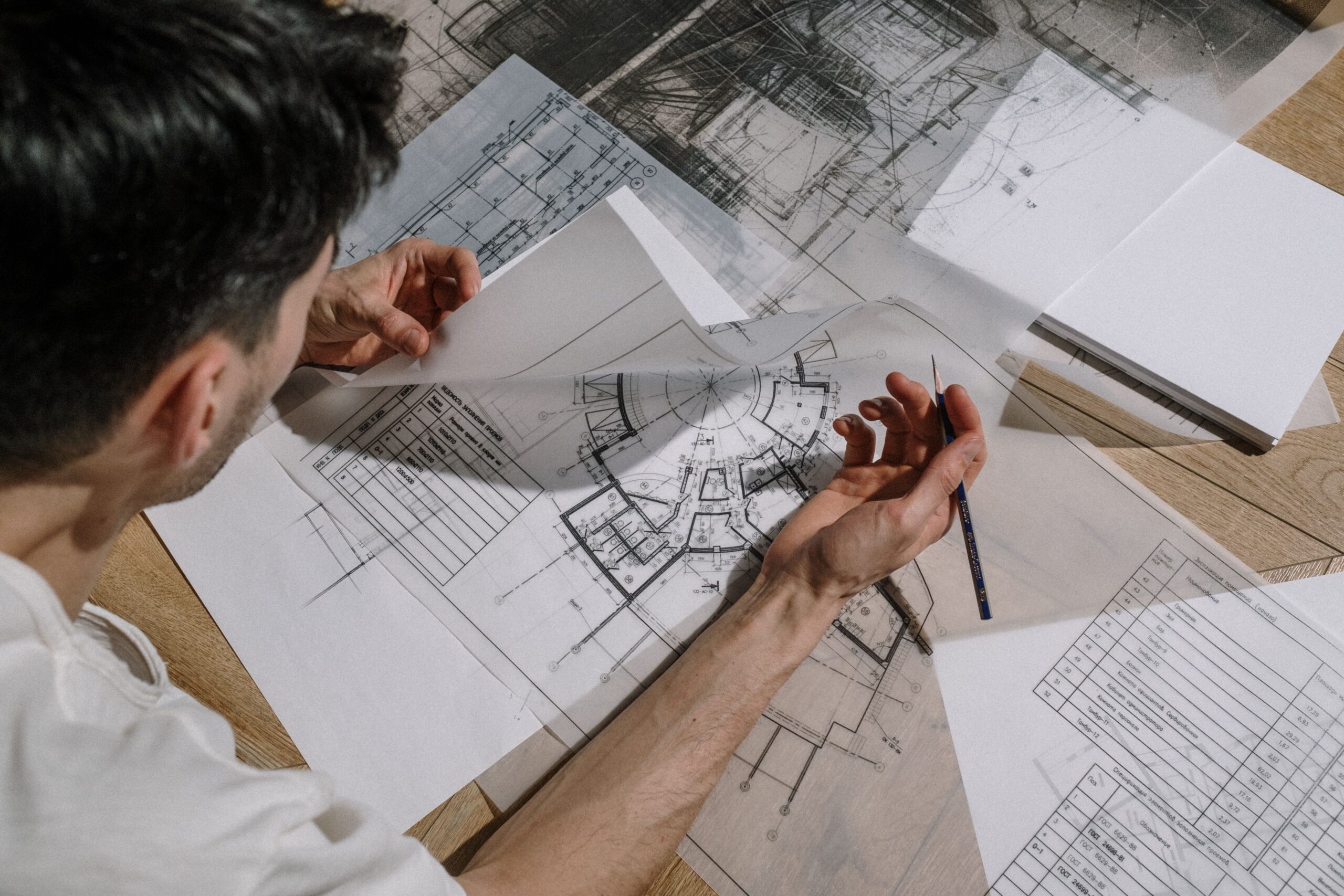 Architect studying and sketching over detailed architectural blueprints indoors.